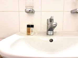 A white bathroom sink with a chrome faucet, two bottles of Argan oil, and a glass soap dispenser on the wall. - Devin (Geneva)