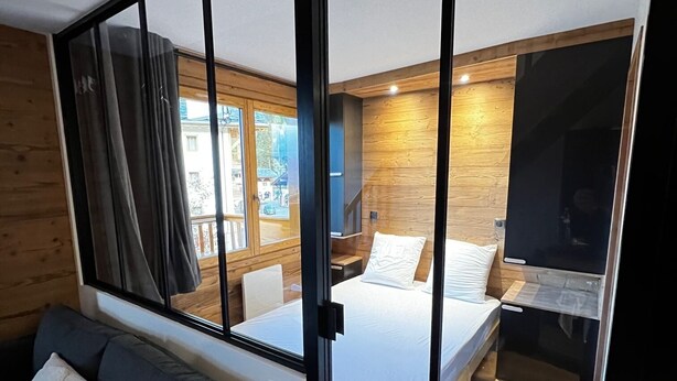 Un dormitorio moderno con un ventanal grande, una cama, una mesita de noche y un sofá.