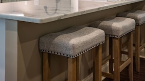 Una cocina con encimera de mármol, taburetes de madera, un grifo negro y un jarrón con flores.
