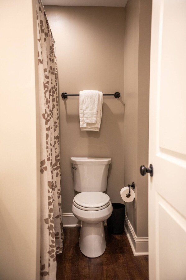 A small, clean bathroom with a toilet, a towel rack, and a shower curtain. - The Dodge, Cozy 1BR King by Velvet Ditch Villas (Oxford)