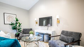 Una sala de estar moderna con un sofá, sillones, una mesa de centro de vidrio, un televisor y una chimenea de mármol.