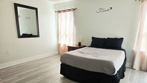 Een slaapkamer met een bed, nachtkastje, spiegel en een muur met een 'Travel'-bord.