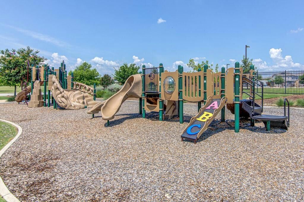 A playground with various play structures, including slides and climbing elements, surrounded by a gravel area.