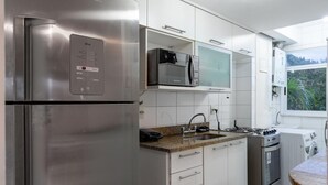 A modern kitchen with stainless steel appliances, white cabinetry, and a view of greenery outside. - Beauty at Recreio For 5 Peopple Sa201 (Rio de Janeiro)