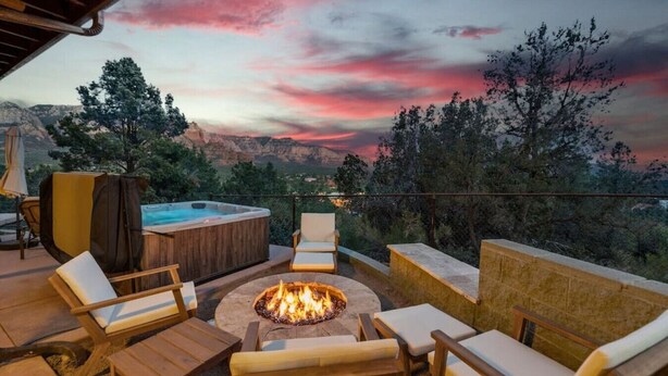 Een terras met buitenmeubilair, een vuurkorf en een hottub met uitzicht op een bergachtig landschap tijdens de zonsondergang.