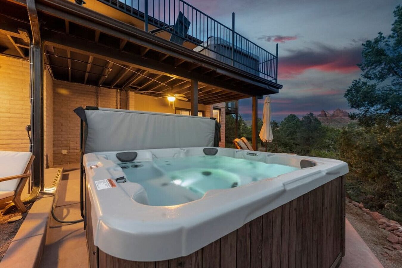 Ein Whirlpool mit Holzaußenverkleidung, ein Balkon mit Geländer und ein Sonnenuntergang im Hintergrund.