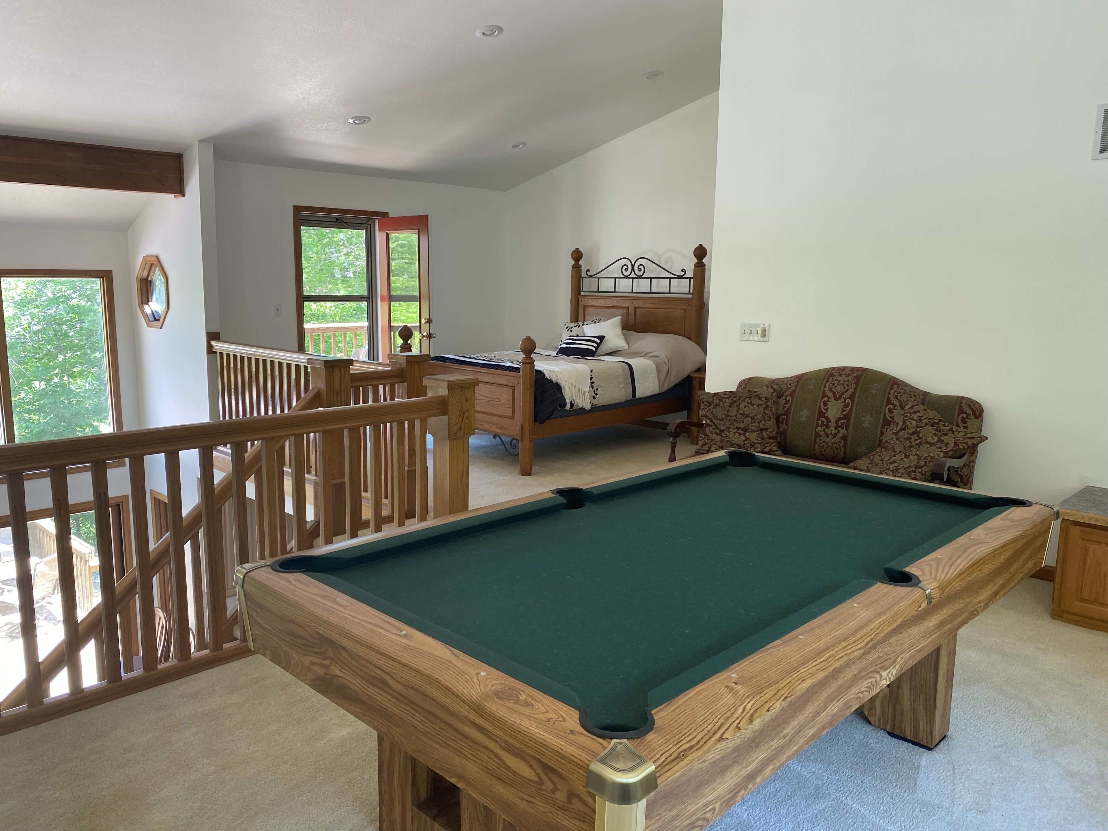 Une pièce comprenant une table de billard, un lit, un canapé et un balcon avec une balustrade.