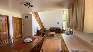 A spacious kitchen with wooden cabinets, a dining area with a wooden table and chairs, a sofa, and a staircase leading to another level. - Riverside/Fishing/Arcade/Pool Table/Disk Golf/Fire Pit/Basketball/Pets/WiFi/UTV (Marion)