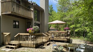 A two-story house with a wooden deck, outdoor furniture, and hanging flower baskets. - Riverside/Fishing/Arcade/Pool Table/Disk Golf/Fire Pit/Basketball/Pets/WiFi/UTV (Marion)