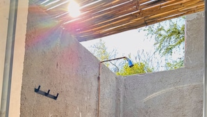 A bathroom with a concrete wall, a shower with a wooden handle, a black faucet, and a potted plant. - Glamping Xochitepec (Xochitepec)