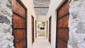 A narrow corridor with stone walls and wooden doors, leading to an outdoor area with a view of trees. - Glamping Xochitepec (Xochitepec)