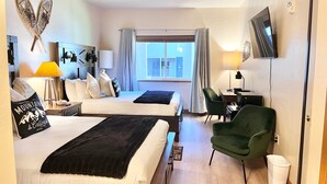 Une chambre d’hôtel avec deux lits, un bureau avec une chaise, une télévision et une fenêtre avec des rideaux.