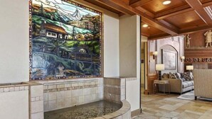 Une salle de bain carrelée de pierre, avec un mur décoré de mosaïques, une baignoire et un plafond en bois.