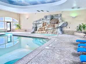 Ein Hallenbad mit Felswand, transparenter Decke und blauen Liegestühlen.
