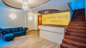 Een receptiegedeelte met een bordje voor 'CENTRAL HOTEL FUVAHMULAH', een houten trap en een bank.
