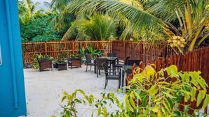 Een tropisch buitenzitgedeelte met tafels en stoelen, omgeven door een bamboomborduurwerk en palmbomen.