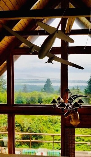 Enjoy a serene view of the lush landscape from the large window in this room, featuring a sloped wooden ceiling and a unique light fixture.