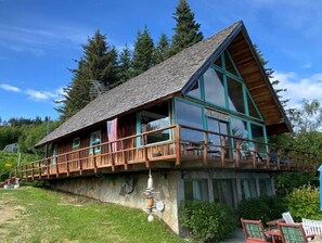 Situated on a grassy slope, this cabin features a two-story design with a steeply pitched roof and large windows.