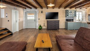 Una sala de estar con una mesa de centro de madera, dos sofás marrones, un televisor y una zona de cocina con armarios y una pared de piedra.