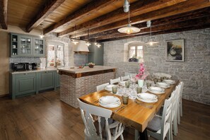 A rustic kitchen with a wooden island, stone walls, and a dining area set for six.