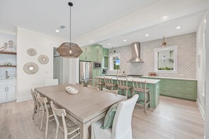 A modern kitchen with a wooden dining table, green cabinets, and stainless steel appliances.