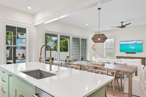 Una cocina moderna con una isla grande, comedor y un televisor montado en la pared.