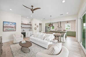 A modern living room with a white sofa, a coffee table, and a dining area with a kitchen in the background.