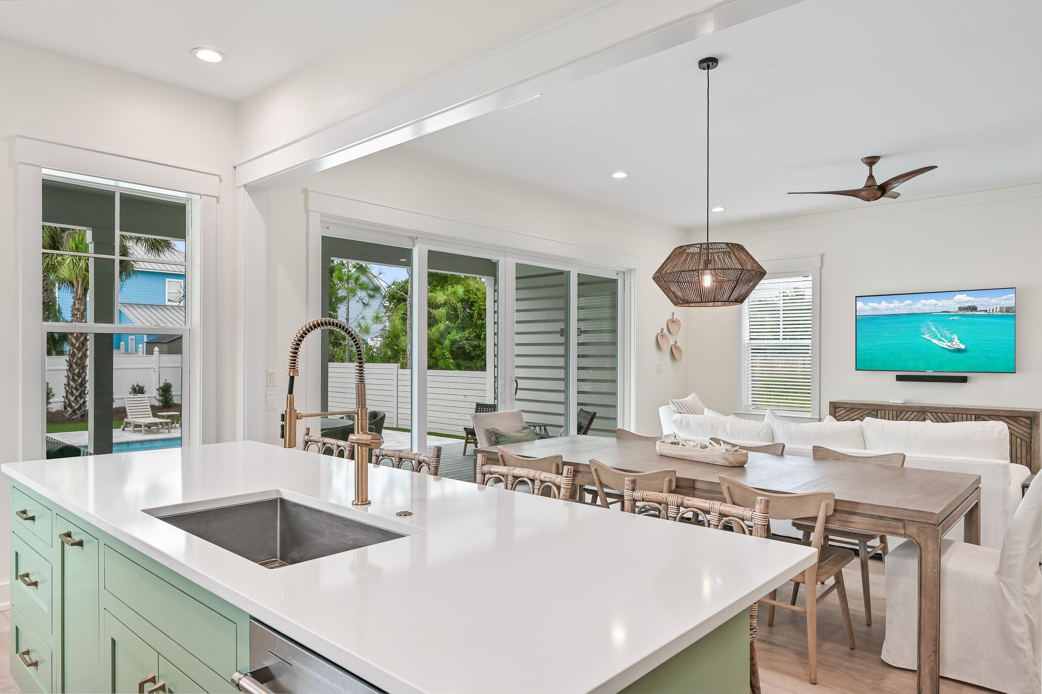 A modern kitchen with a large island, dining area, and a TV mounted on the wall.