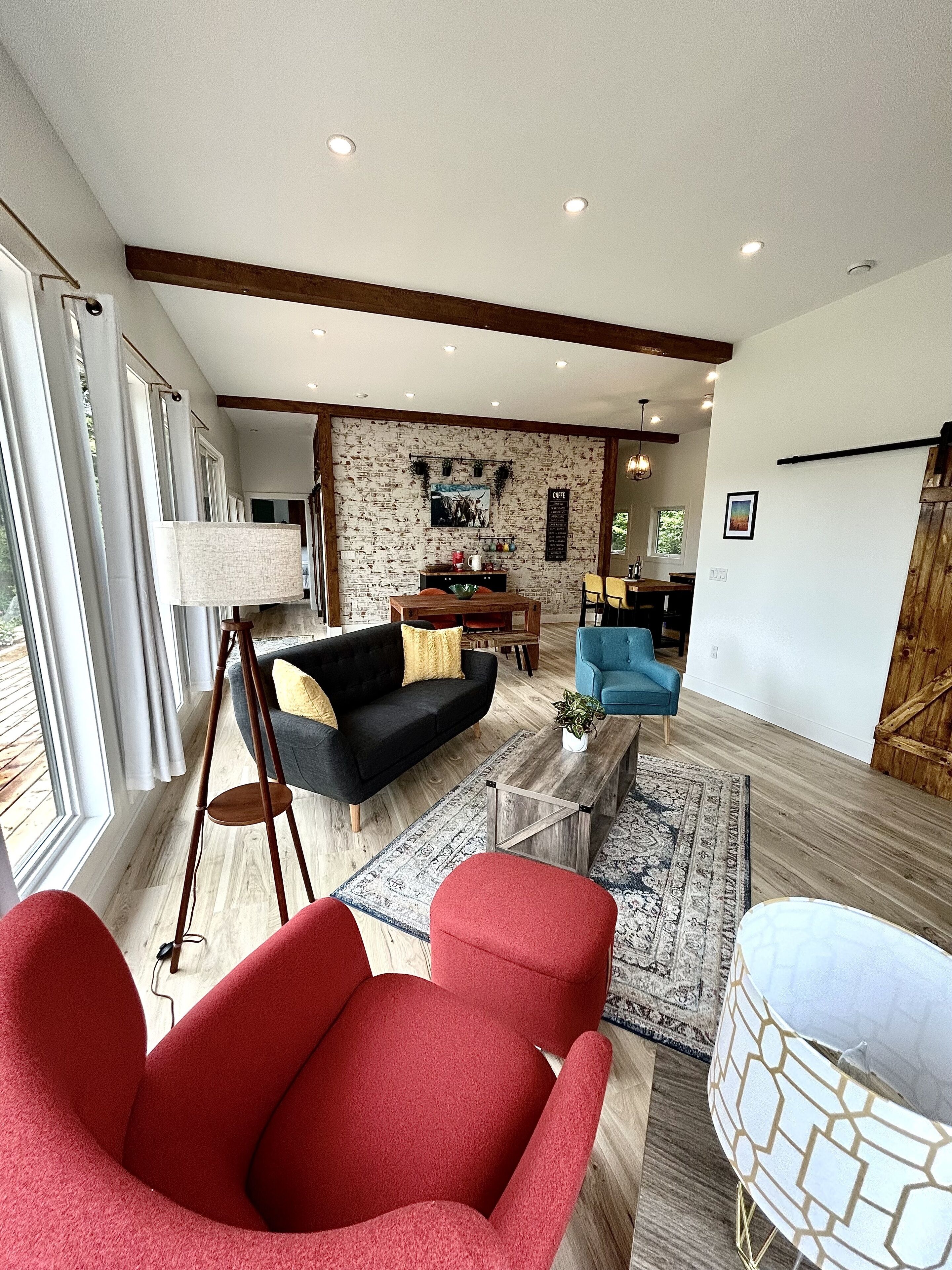 A spacious living area with a black sofa, red armchairs, a wooden coffee table, and a dining area with a blue chair.