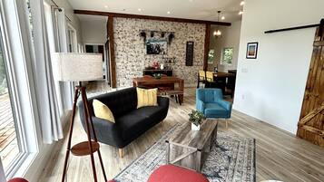 A spacious living area with a black sofa, red armchairs, a wooden coffee table, and a dining area with a blue chair.