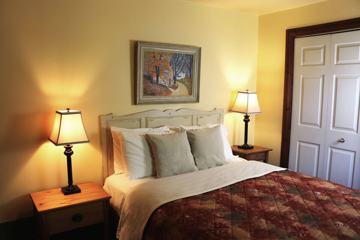 A bedroom with a bed, two bedside tables with lamps, a door, and a painting on the wall.