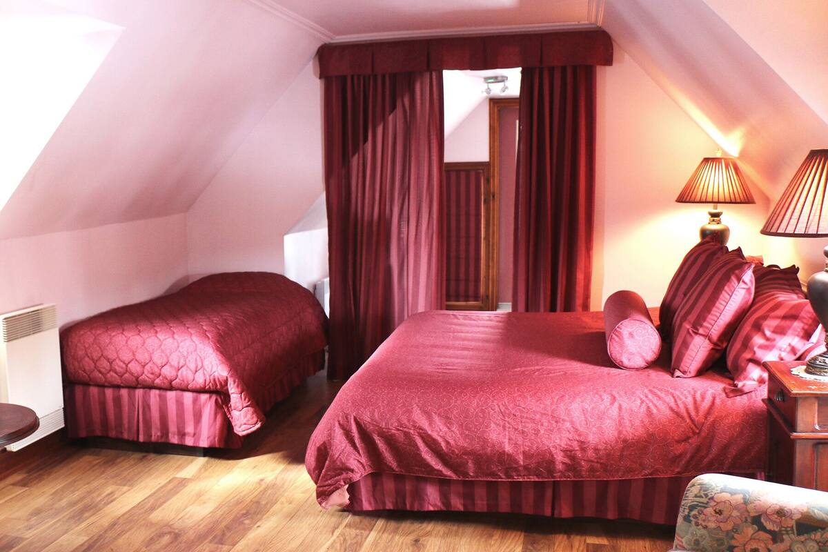 A bedroom with two beds, a wooden floor, a nightstand, and a lamp.