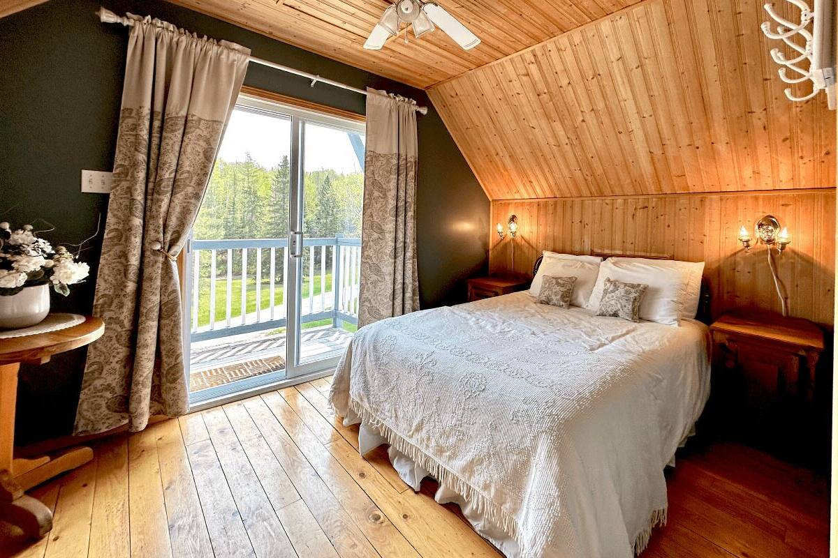 A bedroom with a large bed, wooden floors, a ceiling fan, and a balcony with curtains.