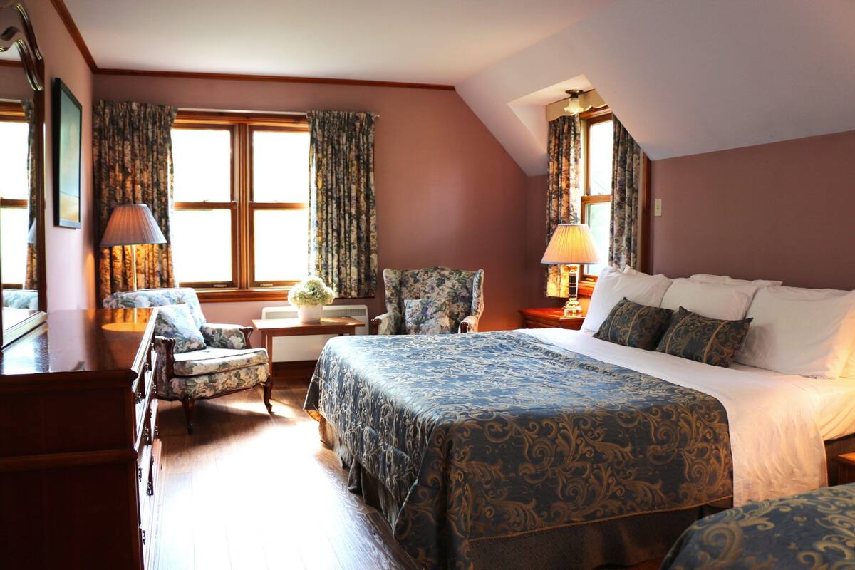 A hotel room with a large bed, a chair, a desk, and a lamp.