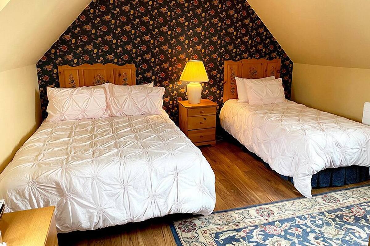 A bedroom with two beds, a nightstand with a lamp, and a floral-patterned wall.