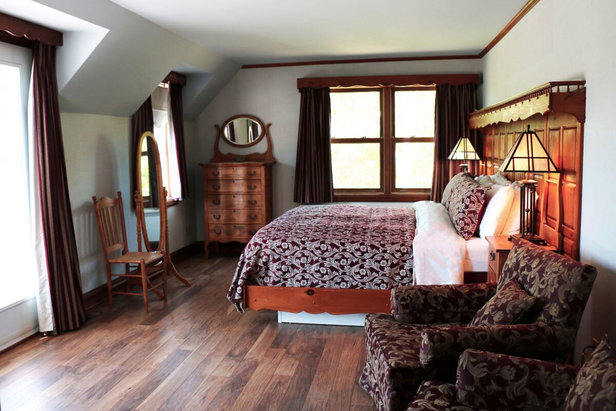 A bedroom with a wooden bed, a dresser, a chair, and a large window.