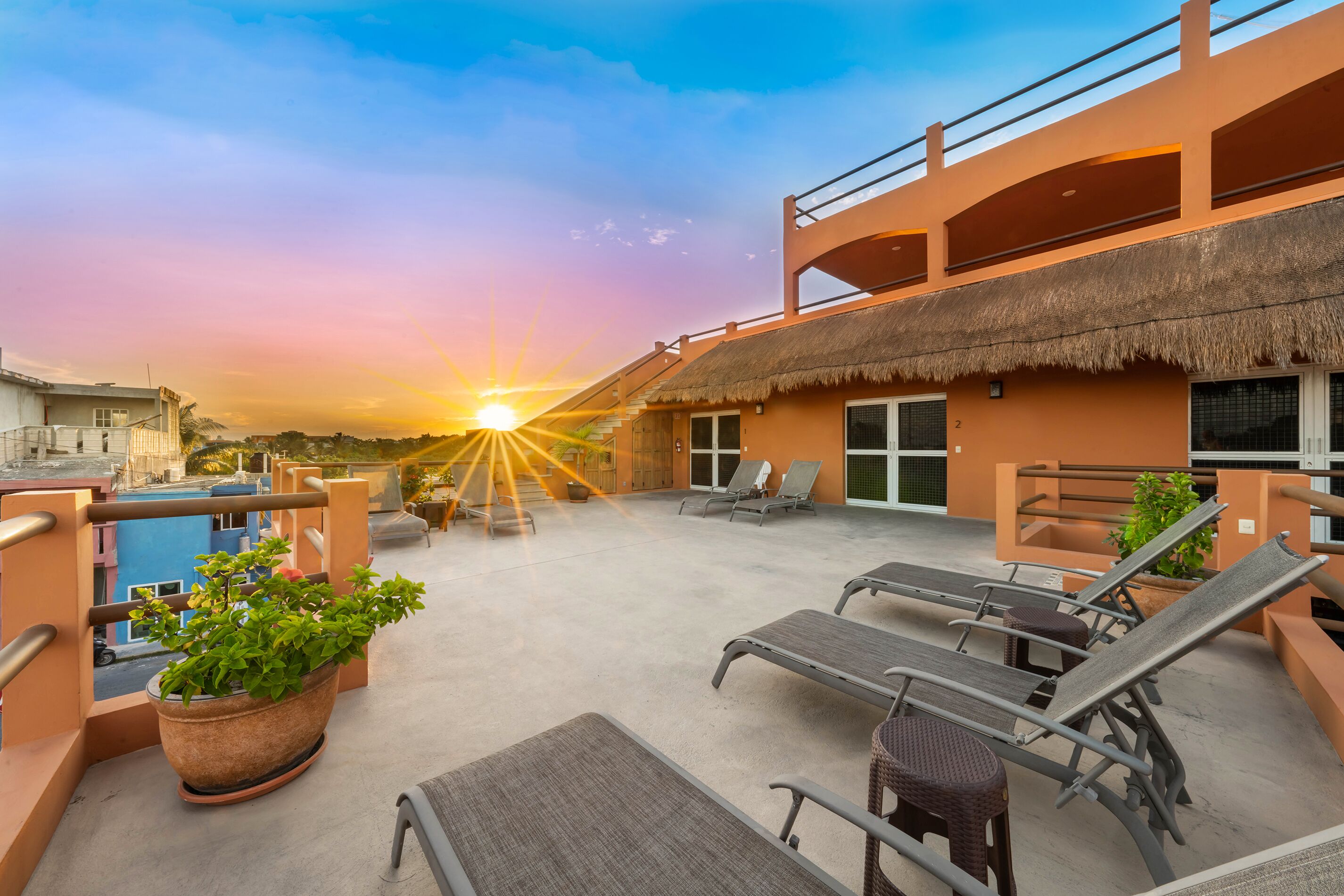 A rooftop terrace with lounge chairs, a pool, and a thatched-roof building.