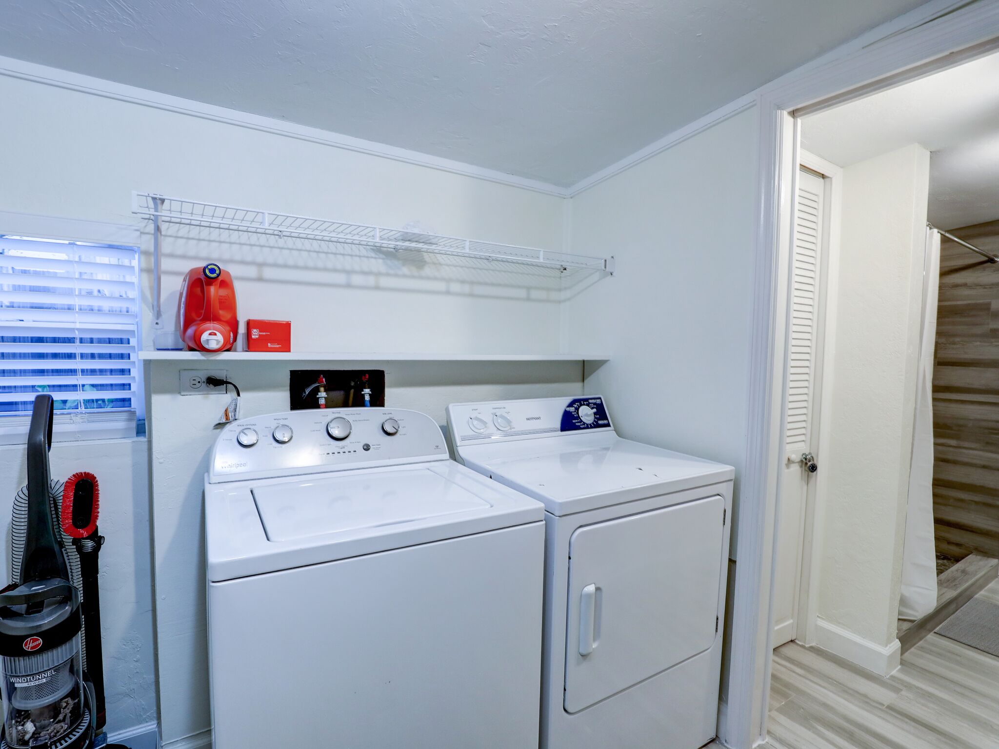 A laundry area with two white front-loading washers and dryers, a red detergent bottle, and a wind tunnel vacuum cleaner.