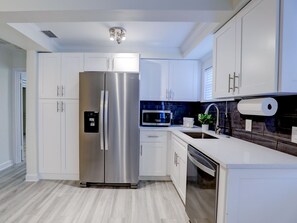 A modern kitchen with white cabinetry, stainless steel appliances, and a wooden floor.