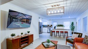 Een moderne woonkamer met een grote flatscreen-tv, een houten salontafel, een rode leren bank en een keuken op de achtergrond.