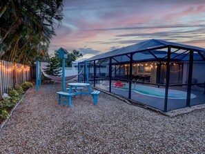 A covered outdoor area with a pool, picnic tables, and string lights.