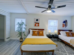 A hotel room with a bed, two bedside tables, a ceiling fan, and a large window with blinds.