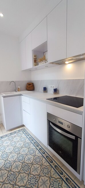 A modern kitchen with white cabinetry, a black countertop, a built-in oven, and a patterned floor.