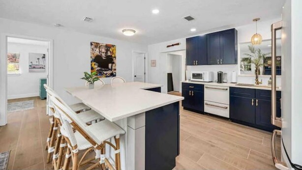 A modern kitchen with dark blue cabinets, a white island, and a dining area with wicker chairs.