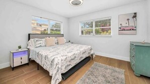 A bedroom with a bed, a nightstand, a dresser, and a window with blinds.