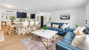 A modern living room with a blue sofa, white coffee table, and wicker chairs.