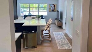 A modern kitchen with a dining area, a trash bin, and a window with a view of the outside.