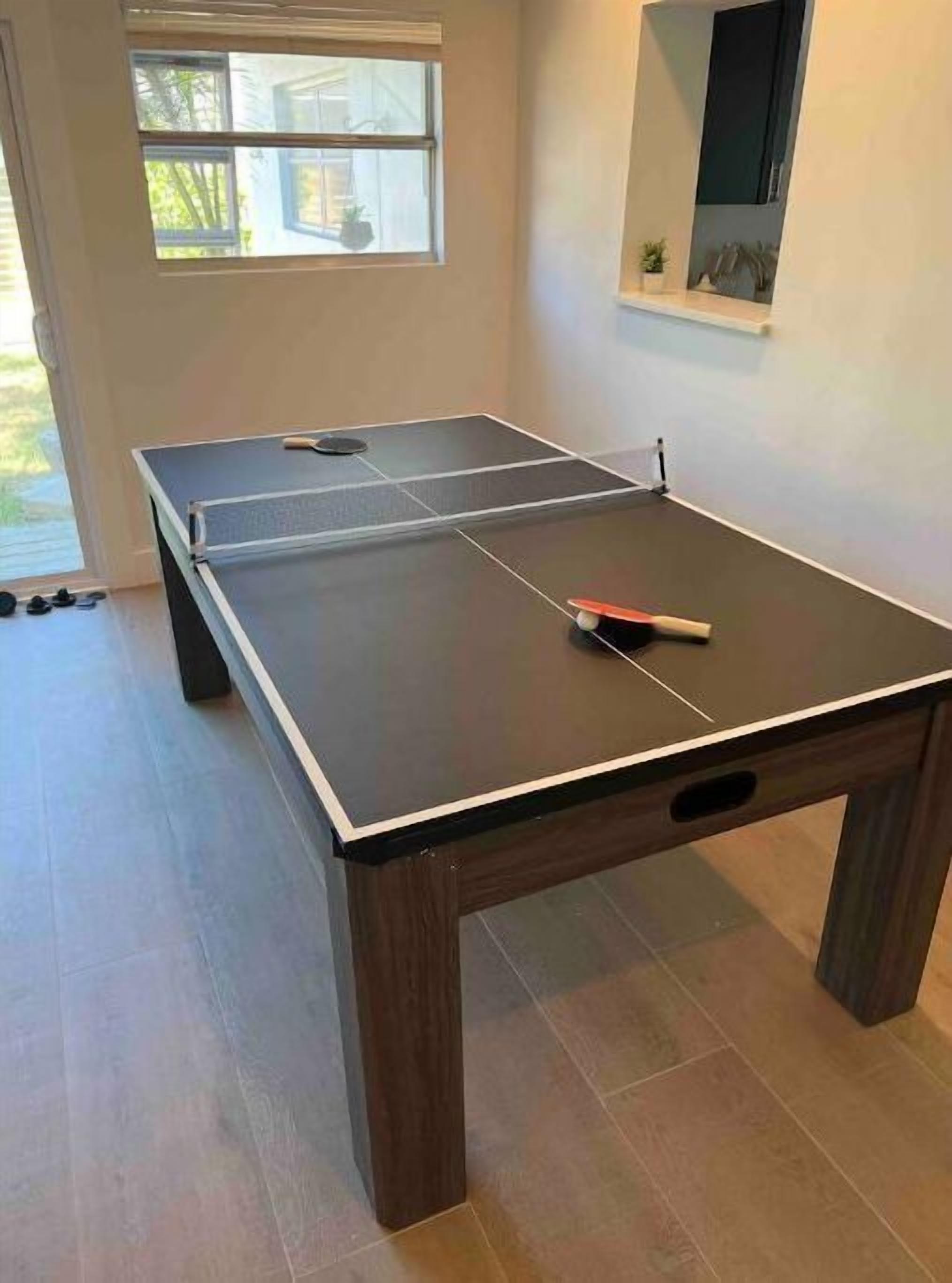 Une table de ping-pong se trouve dans une pièce dotée d’une fenêtre et d’un miroir au mur.
