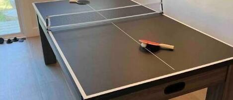 Une table de ping-pong se trouve dans une pièce dotée d’une fenêtre et d’un miroir au mur.