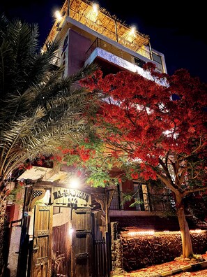 A building with a balcony, a wooden gate, and a tree with red leaves. - Lafamilia Albadwan (Sweimeh)
